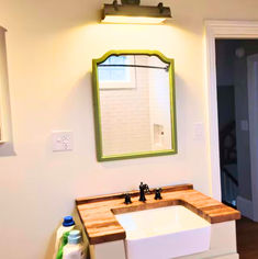 a bathroom sink sitting under a mirror next to a wooden counter top with two faucets