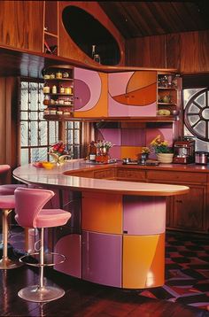 a colorful kitchen with an island and bar stools in the center, surrounded by wood paneling