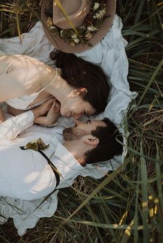 a man and woman laying in the grass with hats on top of their heads together