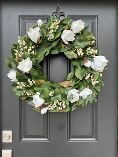 a wreath with white flowers and greenery is hanging on the front door to welcome guests