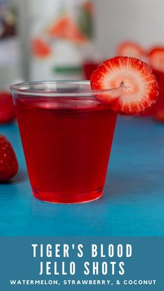 a glass filled with red liquid sitting on top of a blue table next to strawberries