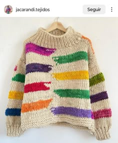 a sweater with multicolored stripes is hanging on a hanger in front of a white wall