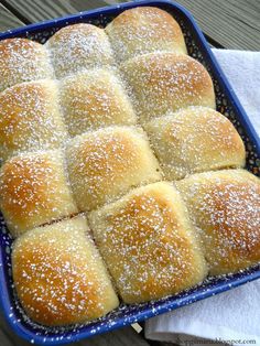 a blue dish filled with rolls covered in powdered sugar on top of a wooden table