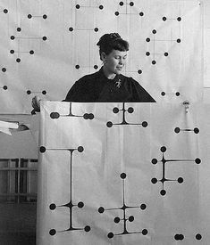 a woman standing behind a white curtain with black dots on it, holding up a large piece of fabric