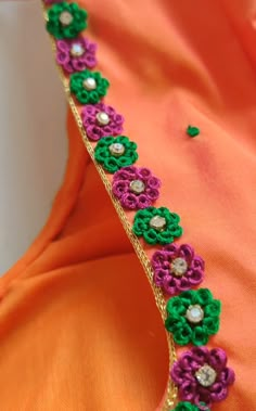 an orange dress with colorful flowers on the side and beads in the center, along with green trim