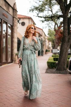 a woman walking down the street in a long green dress and sunglasses with her hand on her hip