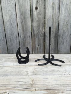 two black wrought iron hooks are on a wooden table next to a fence and wood planks