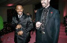 two men in tuxedos standing next to each other at a formal event with pink carpet