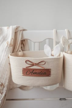 two baskets with name tags on them are hanging from the side of a crib