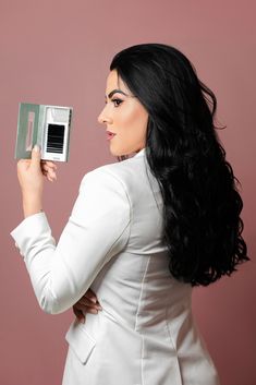 a woman in a white suit holding an electronic device up to her face