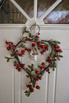 a heart shaped wreath hanging on the front door with bells and holly berries attached to it