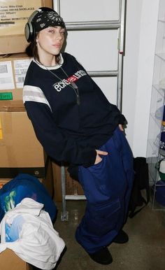 a woman standing in front of boxes with headphones on her ears and wearing blue sweatpants