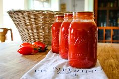 three jars filled with red liquid sitting on top of a table next to a basket