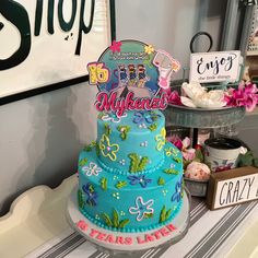 a three tiered cake sitting on top of a table next to a sign and flowers