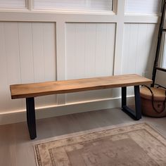 a wooden bench sitting on top of a hard wood floor next to a rug and window