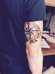 a man's arm with a compass tattoo on it, sitting at a desk