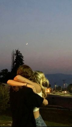 two people hugging each other in front of the moon