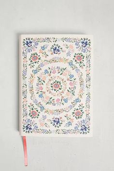 a white notebook with floral designs on the cover and a pink ribbon tied to it