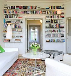 a living room filled with white furniture and lots of books on the shelves above it