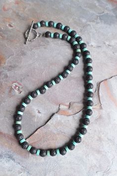 "A beaded mens necklace made with lava rock and turquoise magnesite. The necklace measures 20\". More lengths are listed. The mannequin's neck size is 14.5\". A matching bracelet is also available. Please let us know if you would like to add one to the order. The clasp is gunmetal toggle but a gunmetal lobster claw, stainless steel lobster and lead free pewter toggle are also available. Stainless steel will not tarnish or oxidize and is hypoallergenic. All DLD jewelry comes in a brown kraft pape Black Statement Earrings, J Necklace, Mens Beaded Necklaces, Rock Necklace, Surfer Necklace, Mens Necklace, Turquoise Bead Necklaces, Wood Bead Necklace, Matching Bracelet