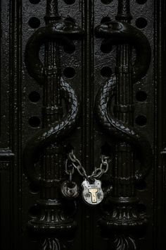 an ornate black door with a lock and chain on the handlebars, in front of a dark background