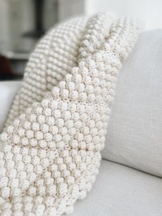 a white knitted blanket sitting on top of a couch next to a gray pillow