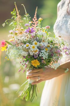 a woman holding a bouquet of wildflowers and daisies in her hands,