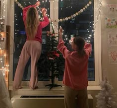 two people standing in front of a window with christmas lights