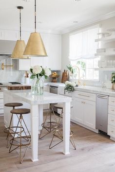 a kitchen with white cabinets and gold pendant lights hanging from the ceiling over the island