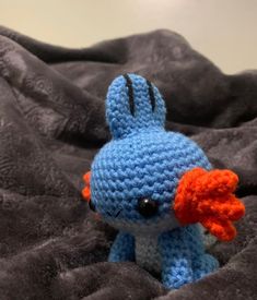 a crocheted blue and orange stuffed animal sitting on top of a black blanket