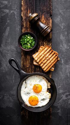 two fried eggs in a frying pan next to toast