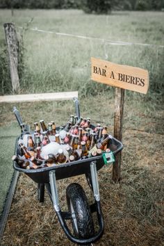 a wheelbarrow filled with beer bottles sitting on top of a grass covered field