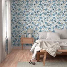 a bedroom with blue flowers on the wall and white bedding in front of it