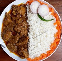 a white plate topped with rice and meat covered in sauce next to carrots and onions