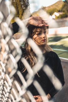 a woman standing behind a chain link fence with her hand on her head and looking at the camera