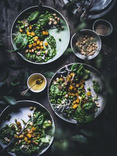 three plates filled with salad on top of a wooden table next to bowls and utensils