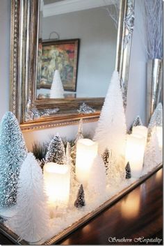 candles are lit in front of small white trees on a table with a mirror behind them