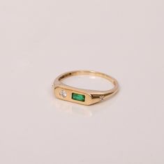 a yellow gold ring with an emerald and diamond set in the middle, sitting on a white surface