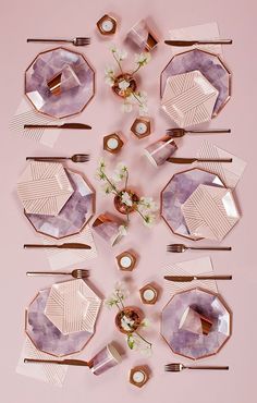 the table is set with pink and gold plates, silverware, flowers and napkins