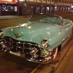 an old car is parked on the side of the road at night in front of a building