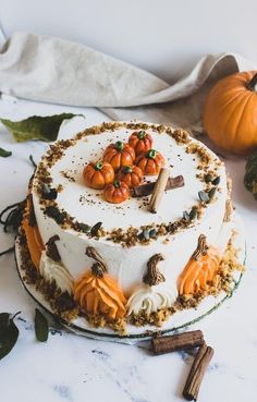 a white cake decorated with pumpkins and leaves on a marble table next to cinnamon sticks