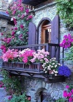 flowers are growing on the balcony of an old stone building with purple shutters and wooden balconies