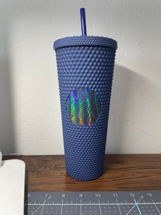 a blue cup sitting on top of a wooden table next to a cutting board and ruler