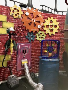 a red brick wall with various colorful gears on it and a gray trash can next to it