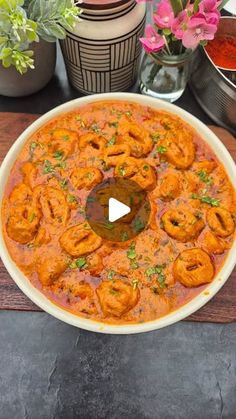 a bowl filled with shrimp and sauce on top of a wooden table next to potted plants