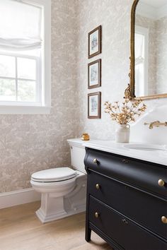 a white toilet sitting next to a black dresser in a bathroom with pictures on the wall