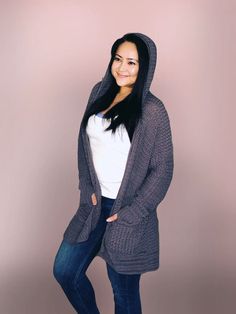 a woman wearing a gray cardigan standing in front of a pink wall with her hands on her hips