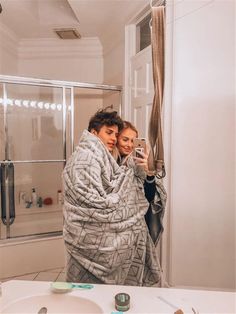 a man and woman wrapped up in blankets taking a selfie in the bathroom mirror