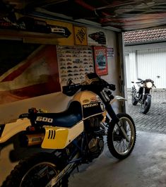 two motorcycles parked in a garage next to each other on the floor and one is yellow