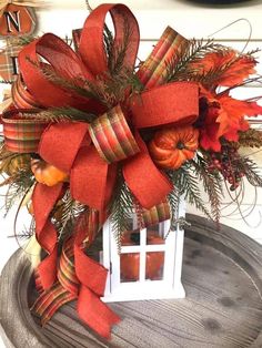 a red bow on top of a white lantern with orange flowers and pine cones in it